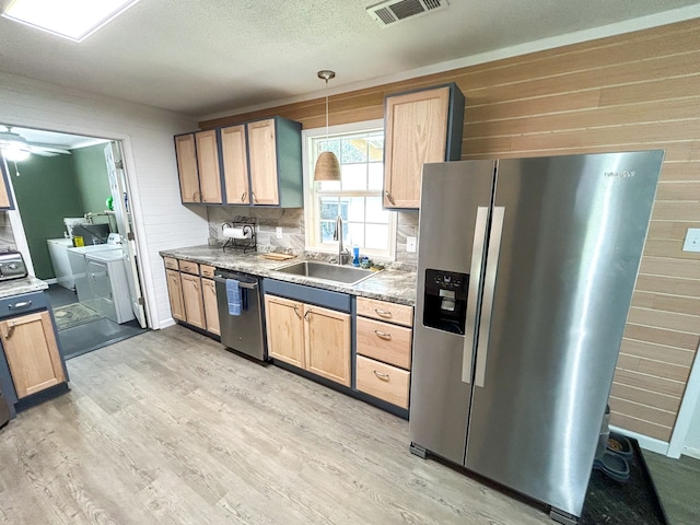 kitchen featuring washer and dryer, stainless steel appliances, sink, hanging light fixtures, and light wood-type flooring