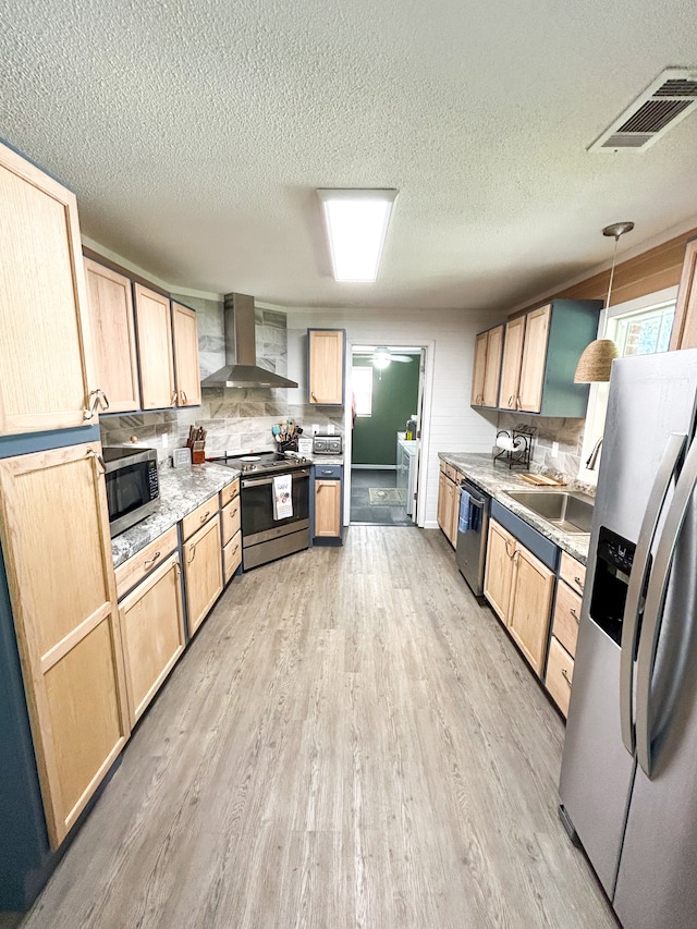 kitchen with light brown cabinets, pendant lighting, wall chimney range hood, and stainless steel appliances