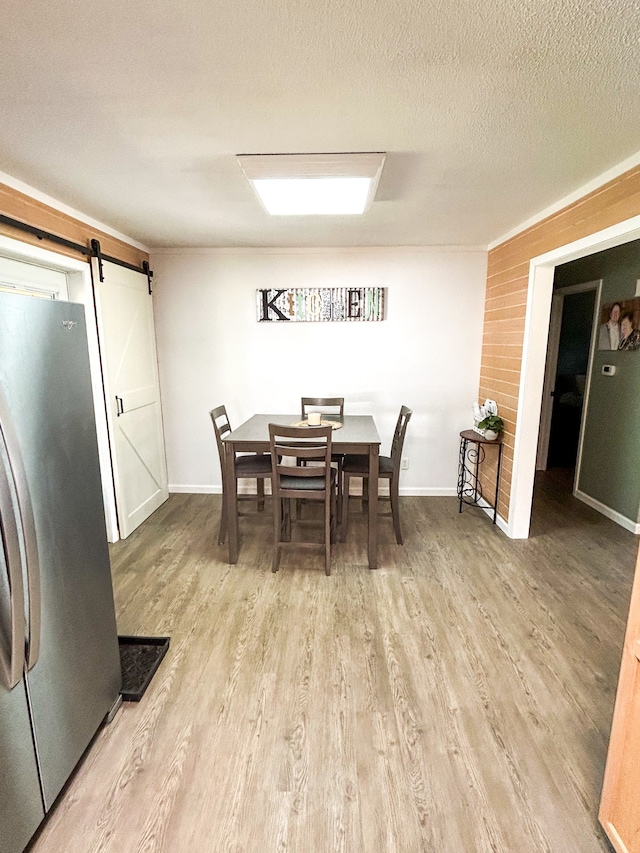 dining space with a barn door, light hardwood / wood-style floors, and a textured ceiling