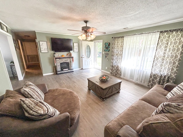 living room with ceiling fan, a stone fireplace, light hardwood / wood-style flooring, and a textured ceiling