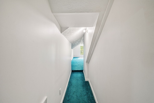 hallway with vaulted ceiling, dark colored carpet, and a textured ceiling