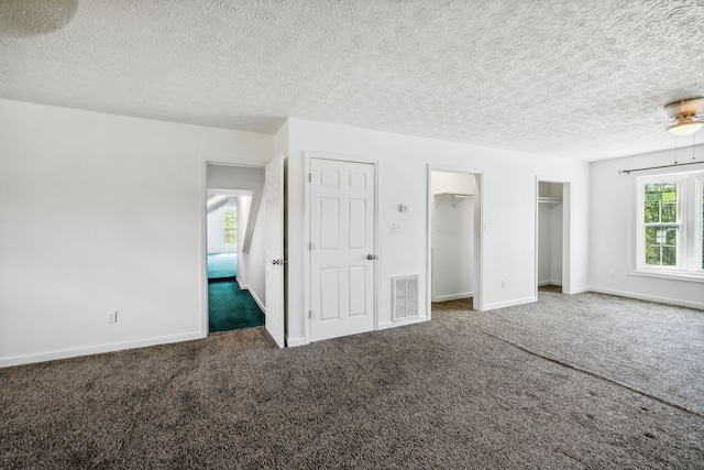 unfurnished bedroom featuring a spacious closet, dark colored carpet, multiple windows, and a textured ceiling