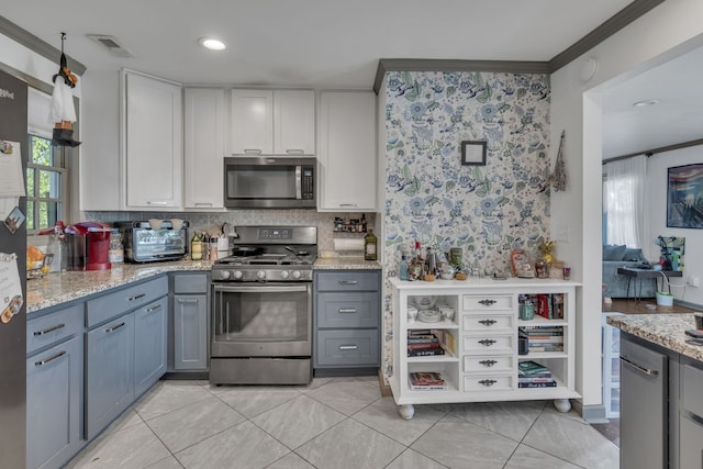 kitchen with decorative backsplash, appliances with stainless steel finishes, light stone countertops, gray cabinets, and crown molding