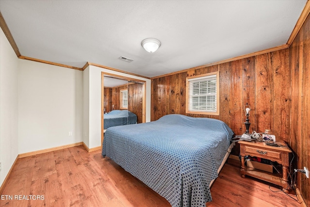 bedroom featuring a closet, light hardwood / wood-style flooring, wood walls, and ornamental molding