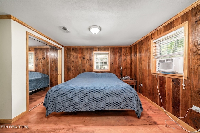 bedroom featuring wood walls, a closet, ornamental molding, hardwood / wood-style flooring, and a textured ceiling