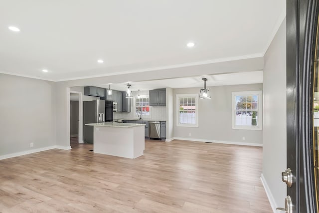 kitchen featuring light wood-type flooring, tasteful backsplash, ornamental molding, stainless steel appliances, and gray cabinets