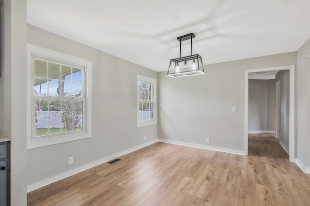 unfurnished dining area with light wood-type flooring, a healthy amount of sunlight, and a notable chandelier