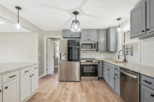 kitchen featuring sink, light hardwood / wood-style flooring, decorative light fixtures, decorative backsplash, and appliances with stainless steel finishes