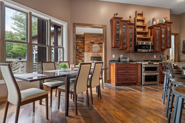 kitchen featuring dark wood-type flooring, a stone fireplace, appliances with stainless steel finishes, and dark stone countertops