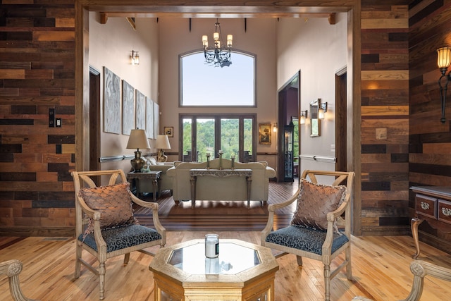 living area with wood walls, a towering ceiling, a chandelier, and light wood-type flooring