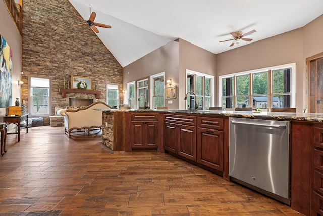 kitchen featuring stainless steel dishwasher, high vaulted ceiling, dark hardwood / wood-style floors, dark stone countertops, and a stone fireplace