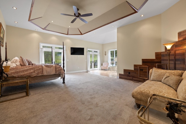 carpeted bedroom featuring a towering ceiling, access to outside, ceiling fan, and a raised ceiling