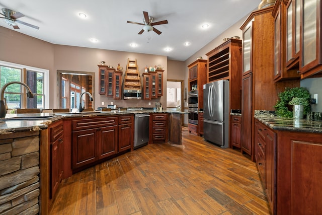 kitchen featuring sink, ceiling fan, stainless steel appliances, dark wood-type flooring, and dark stone countertops