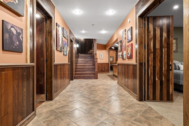 hallway featuring wooden walls, a textured ceiling, and light colored carpet