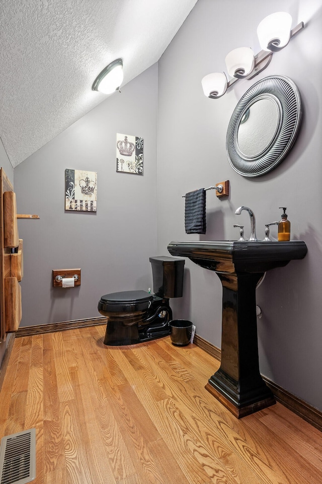 bathroom with toilet, a textured ceiling, vaulted ceiling, and hardwood / wood-style floors