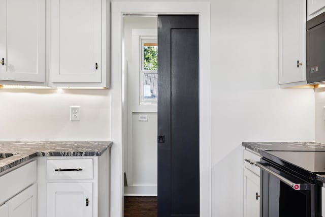 kitchen with white cabinetry, stainless steel range with electric cooktop, and dark stone countertops