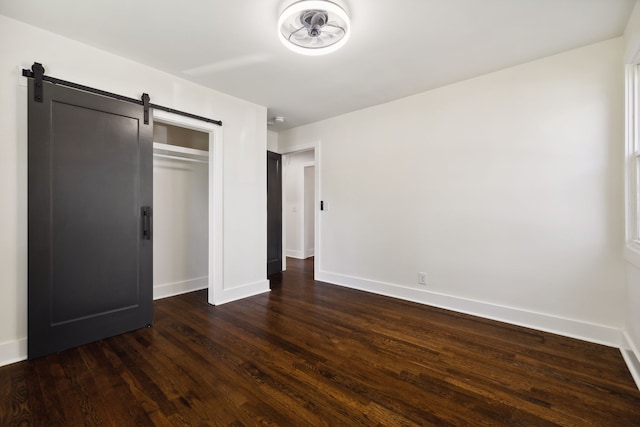 unfurnished bedroom with a closet, dark hardwood / wood-style floors, and a barn door