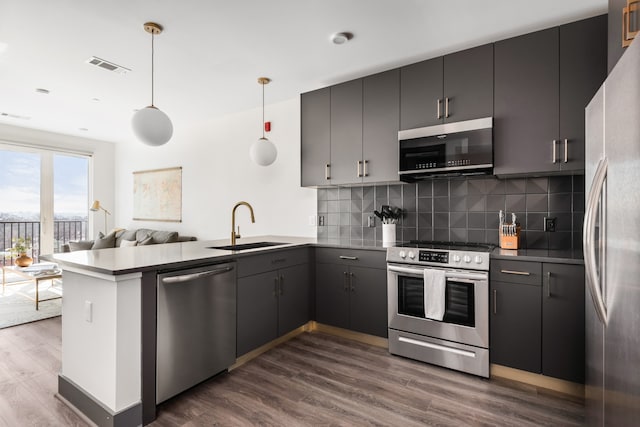 kitchen with sink, kitchen peninsula, decorative light fixtures, stainless steel appliances, and dark hardwood / wood-style flooring