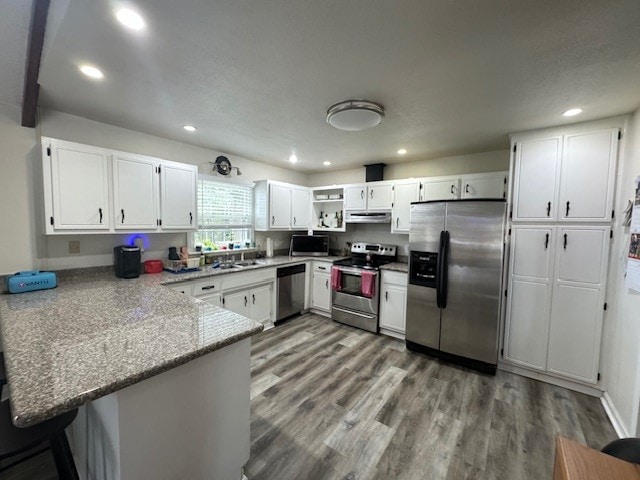 kitchen featuring stainless steel appliances, kitchen peninsula, light stone countertops, and white cabinetry