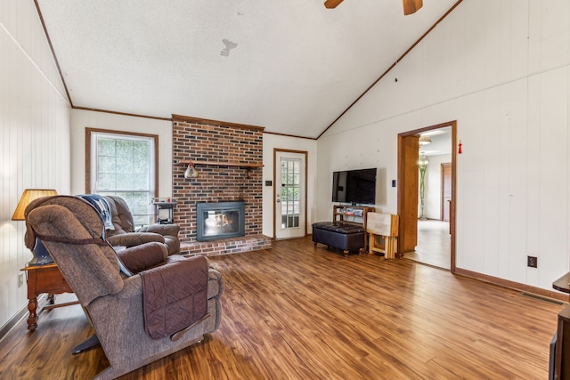 living room featuring high vaulted ceiling, wood-type flooring, ornamental molding, ceiling fan, and a brick fireplace