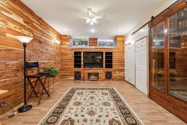 living room featuring a barn door, wood walls, light hardwood / wood-style floors, and ceiling fan