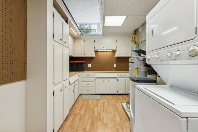 kitchen featuring a paneled ceiling, stacked washer / dryer, light hardwood / wood-style flooring, and white cabinets