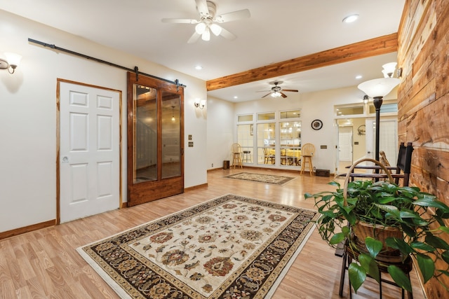 interior space featuring a barn door, beam ceiling, light wood-type flooring, and ceiling fan