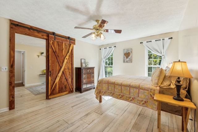 bedroom featuring ceiling fan, light hardwood / wood-style flooring, a barn door, and multiple windows