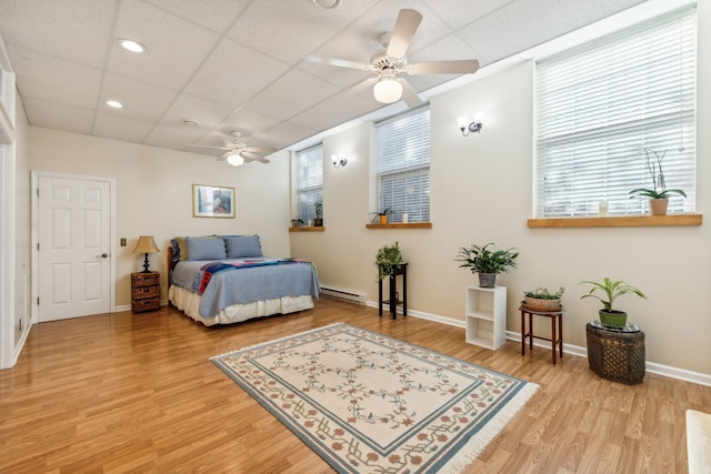 bedroom featuring a drop ceiling, light hardwood / wood-style floors, a baseboard heating unit, and ceiling fan