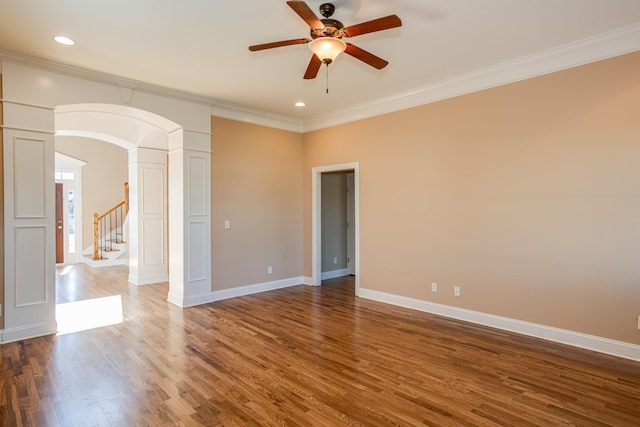 unfurnished room featuring baseboards, ornate columns, a ceiling fan, wood finished floors, and crown molding