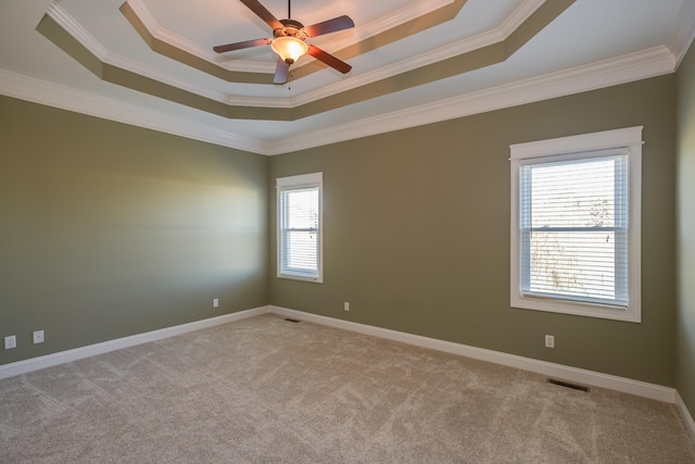empty room featuring a tray ceiling, light carpet, a ceiling fan, and ornamental molding