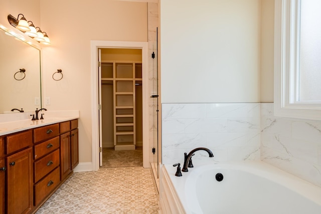 full bath featuring tile patterned floors, a sink, double vanity, a garden tub, and a walk in closet