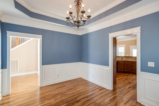 empty room with wood finished floors, wainscoting, an inviting chandelier, ornamental molding, and visible vents