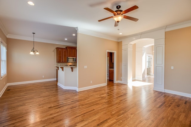 unfurnished living room with arched walkways, light wood finished floors, a ceiling fan, and crown molding