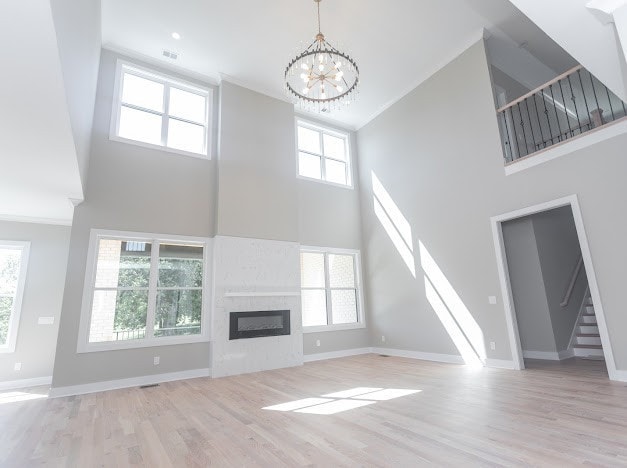 unfurnished living room featuring a notable chandelier, a towering ceiling, light hardwood / wood-style floors, and plenty of natural light