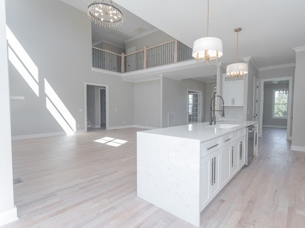 kitchen with white cabinets, hanging light fixtures, sink, a kitchen island with sink, and crown molding