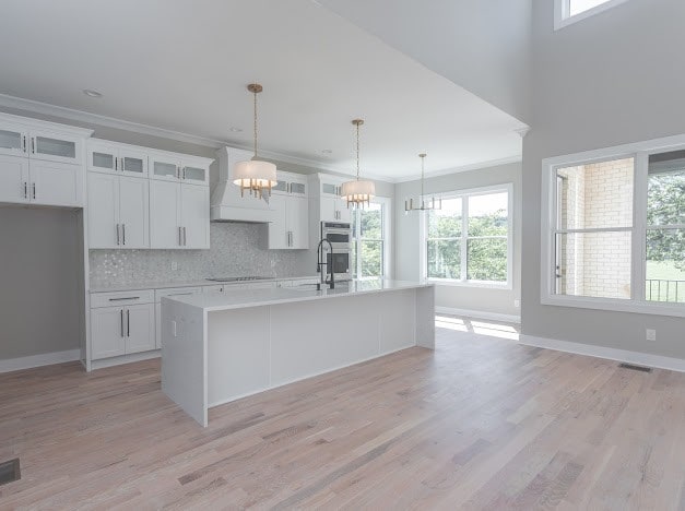 kitchen with a center island with sink, pendant lighting, ornamental molding, and white cabinets