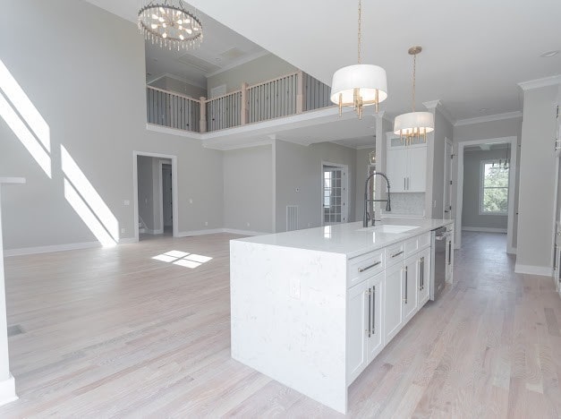 kitchen with a kitchen island with sink, crown molding, light hardwood / wood-style flooring, sink, and hanging light fixtures