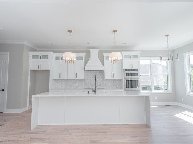 kitchen featuring pendant lighting, an island with sink, and custom range hood