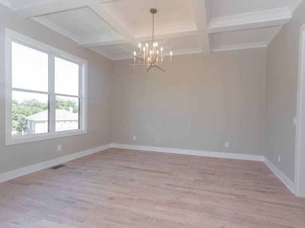 empty room featuring light hardwood / wood-style floors, beamed ceiling, coffered ceiling, and a chandelier