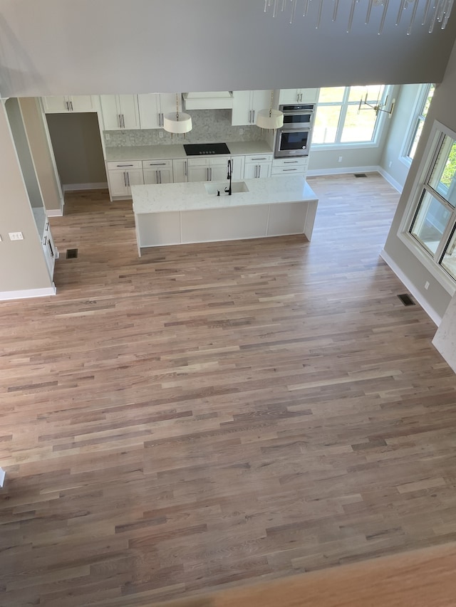 kitchen with light wood-type flooring, white cabinetry, sink, and backsplash