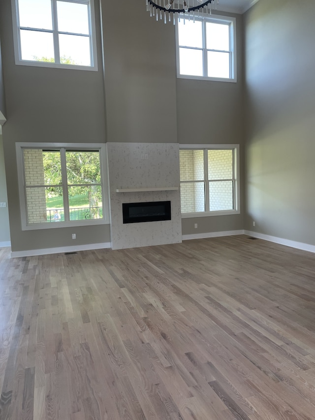 unfurnished living room with a high ceiling, an inviting chandelier, and light hardwood / wood-style floors