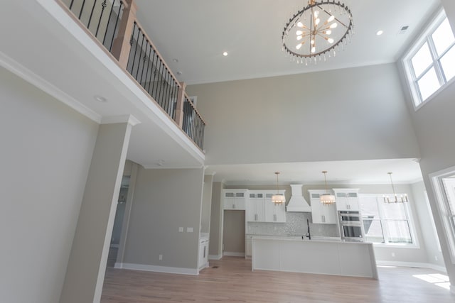 unfurnished living room featuring light hardwood / wood-style floors, an inviting chandelier, a towering ceiling, sink, and ornamental molding