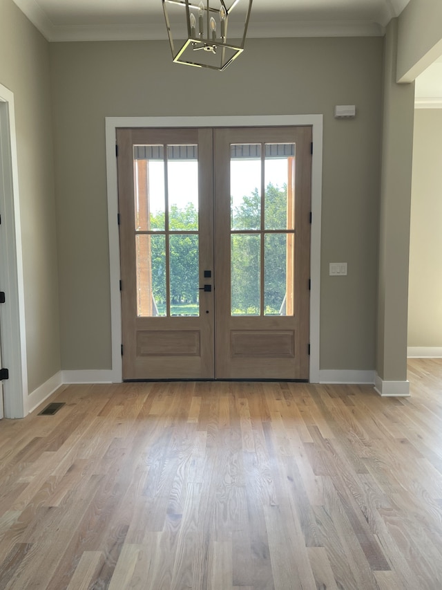 entryway with a healthy amount of sunlight, crown molding, french doors, and light hardwood / wood-style flooring