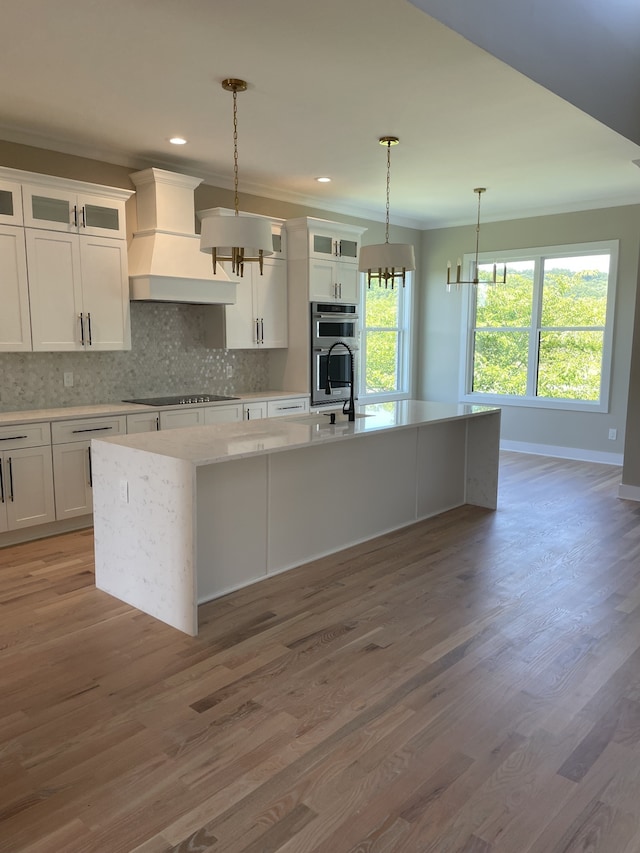 kitchen with custom exhaust hood, decorative light fixtures, a kitchen island with sink, hardwood / wood-style flooring, and stainless steel double oven