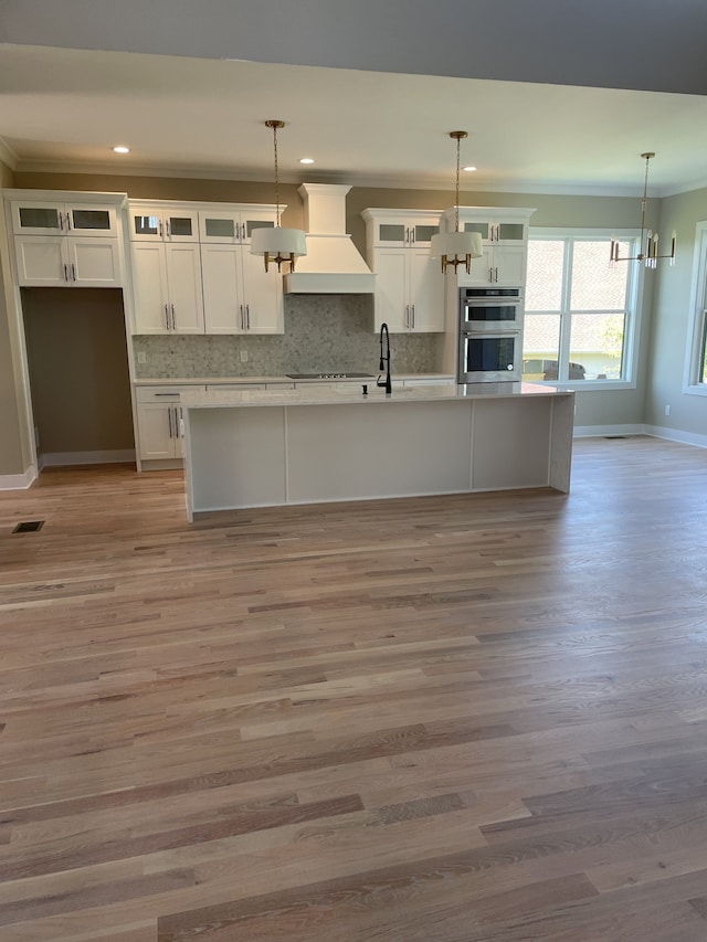 kitchen featuring light wood-type flooring, custom exhaust hood, stainless steel double oven, and hanging light fixtures