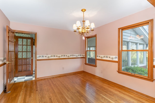 spare room with lofted ceiling, an inviting chandelier, and light hardwood / wood-style floors