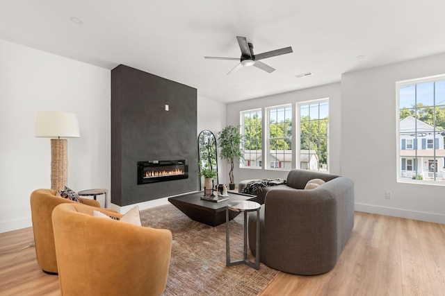 living room featuring light wood-type flooring, ceiling fan, and a large fireplace