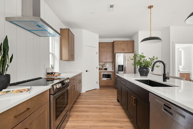 kitchen featuring hanging light fixtures, sink, wall chimney range hood, appliances with stainless steel finishes, and light hardwood / wood-style floors