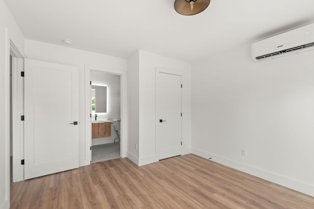 unfurnished bedroom featuring an AC wall unit, ensuite bath, a closet, and light hardwood / wood-style floors